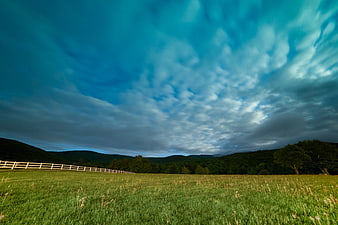 Dramatic Blue Sky Over Green Pasture with White Fence