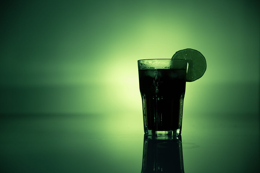 Dark cocktail with lime slice on green background