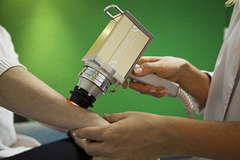 Medical professional using laser device for skin treatment on patient arm