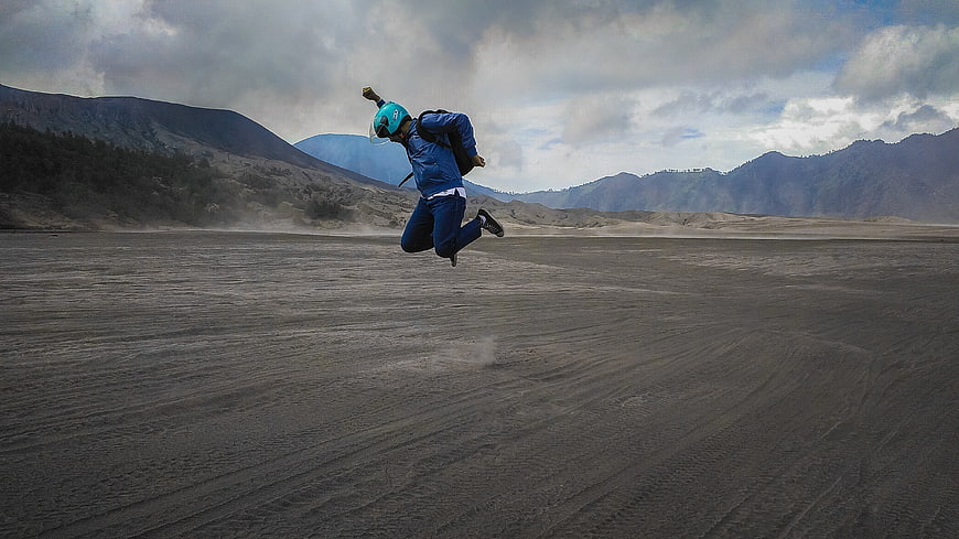 Man jumping in blue jacket at Mount Bromo volcanic sand sea