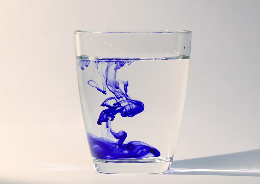 Blue ink diffusing in a glass of water on a white background