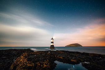 Lighthouse on Rocky Coast Under Starry Night Sky