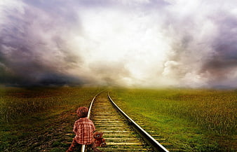 Child with teddy bear sitting on railroad tracks in misty meadow