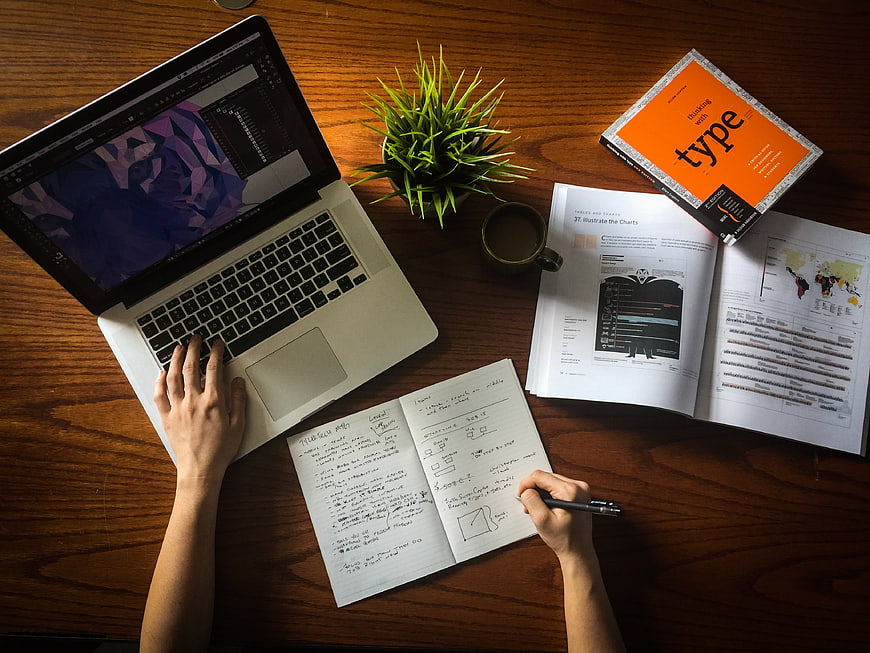 Top-Down View of Designer Workspace with Laptop, Sketchbook, and Books