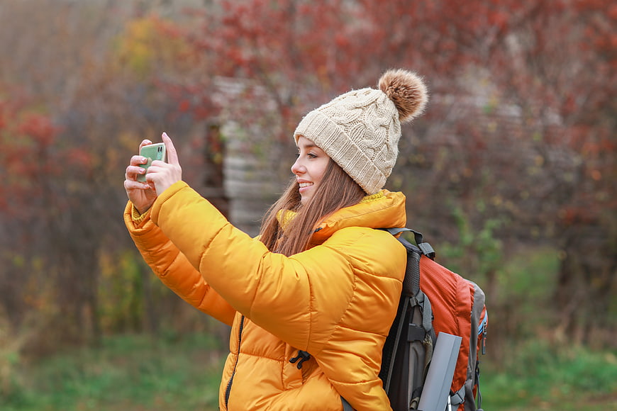 Woman in yellow jacket taking selfie in autumn forest