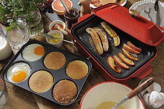 Overhead view of red electric grill cooking breakfast pancakes and eggs