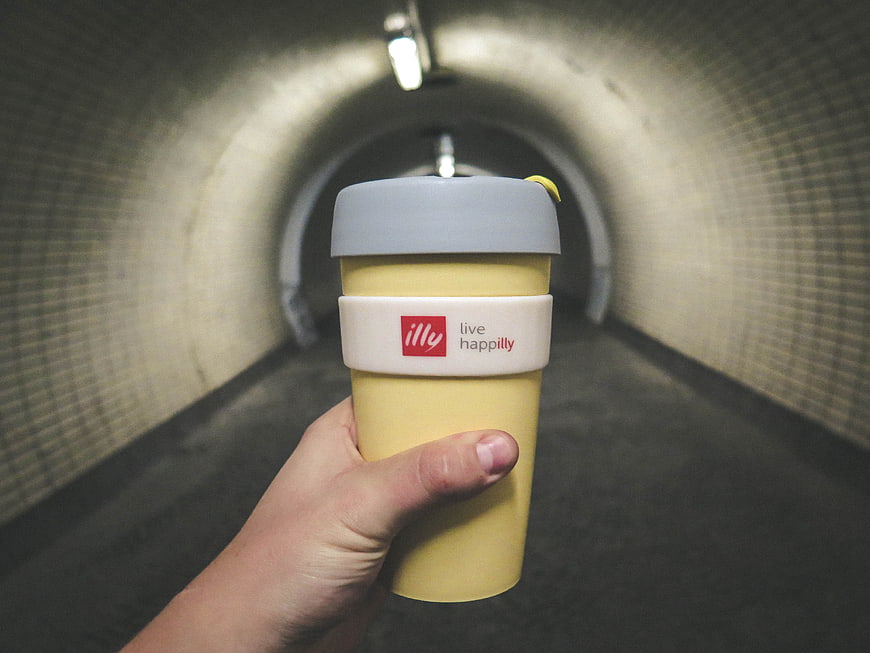 Hand holding yellow illy coffee cup in tiled tunnel
