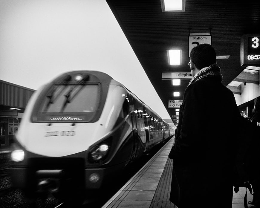 Black and white photo of commuter waiting for train at station platform
