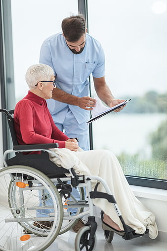 Male nurse discussing medical records with elderly woman in wheelchair
