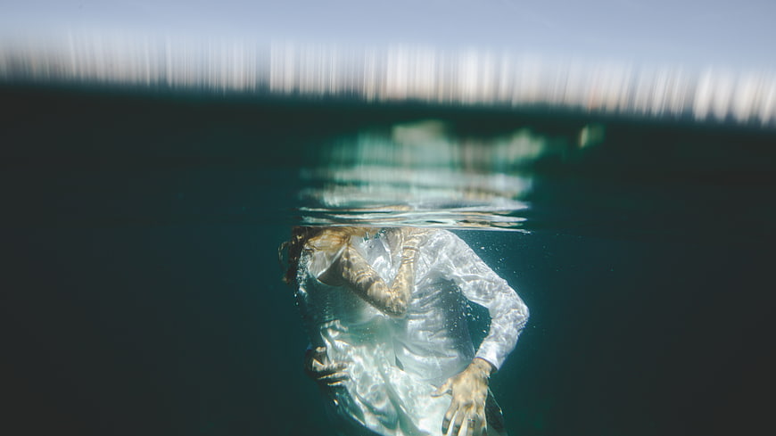 Woman submerged underwater in white dress with light refraction
