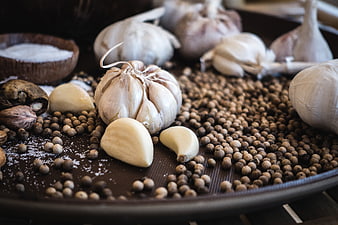 Fresh garlic bulbs and peppercorns on dark wooden board