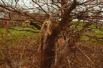 Blonde woman in black dress standing among bare autumn tree branches
