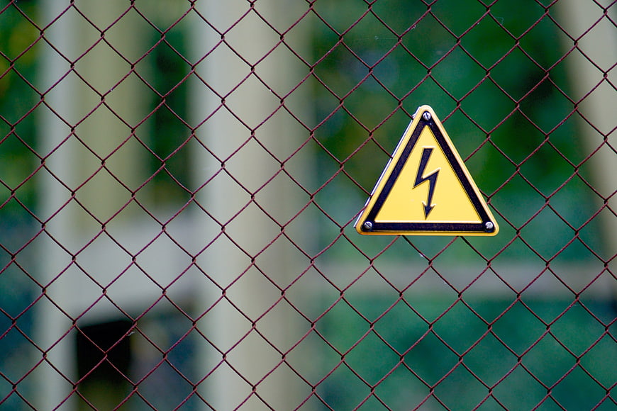 Yellow high voltage warning sign on chain link fence
