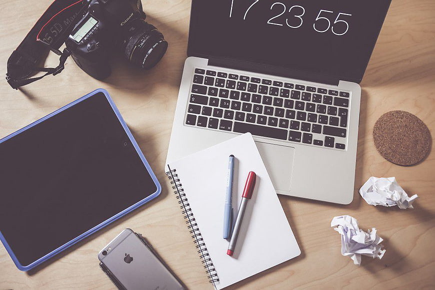 Flat lay workspace with laptop, camera, tablet, and notebook