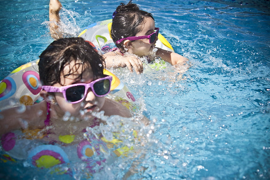 Two young girls swimming and splashing in a pool with floaties