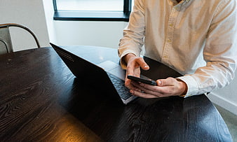 Man using smartphone and laptop at wooden desk