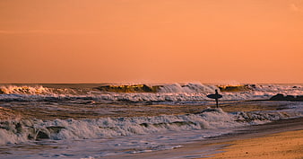 Surfer with board walking into ocean waves at sunset