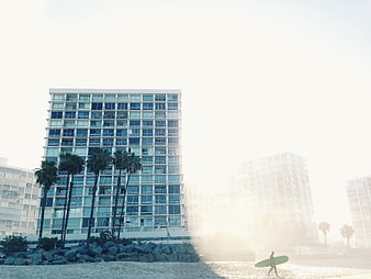 Surfer walking on beach with modern high-rise buildings and palm trees