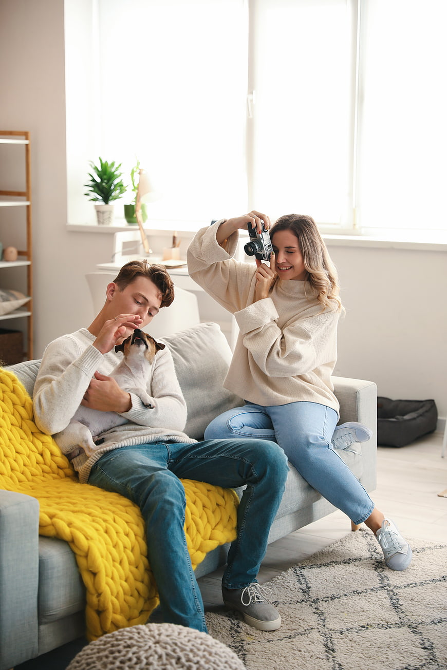 Happy couple taking photo with vintage camera and dog on sofa