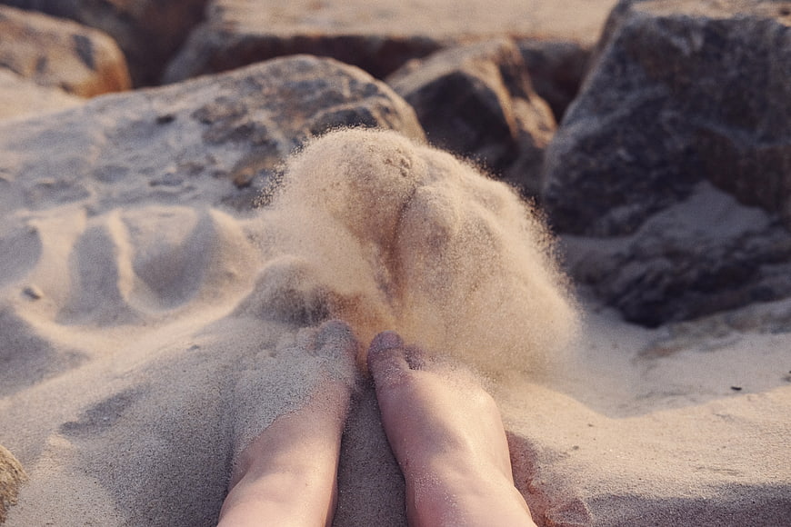 Bare feet kicking sand on a rocky beach shore