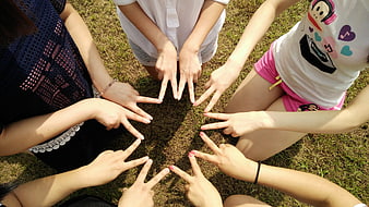 Group of friends making peace signs in a circle on grass