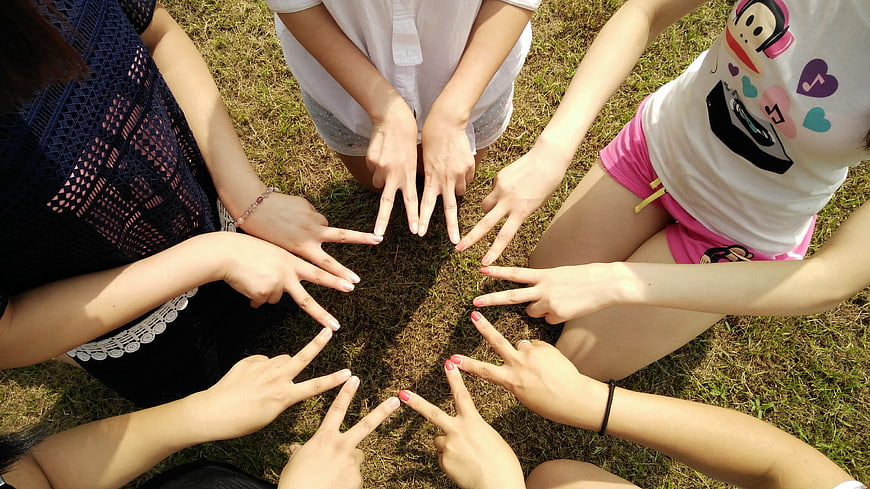 Group of friends making peace signs in a circle on grass
