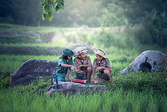 Three young scouts cooking outdoors in a grassy field
