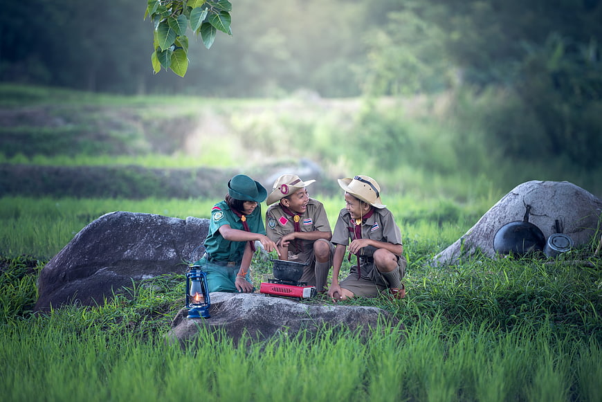 Three young scouts cooking outdoors in a grassy field