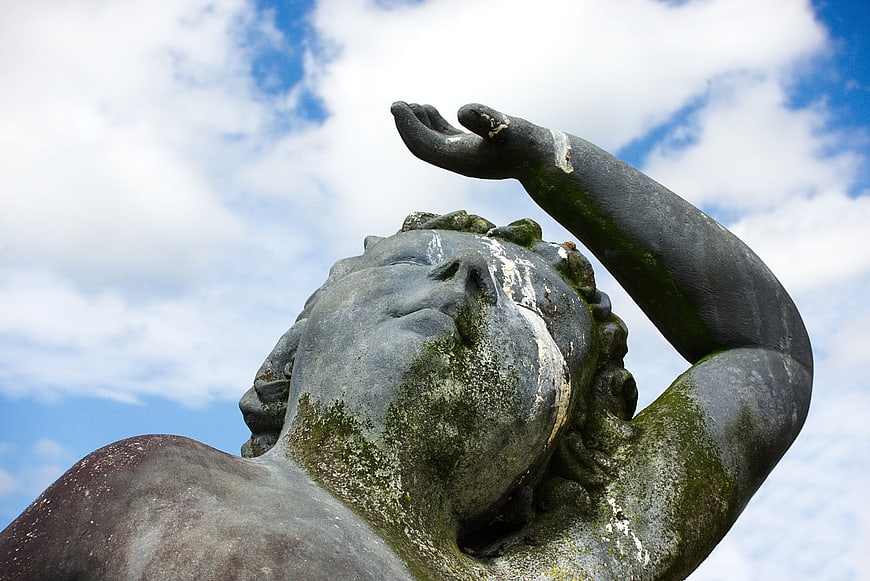 Low angle view of weathered stone cherub statue against blue sky