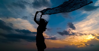 Silhouette of Woman Holding Scarf Against Dramatic Sunset Sky