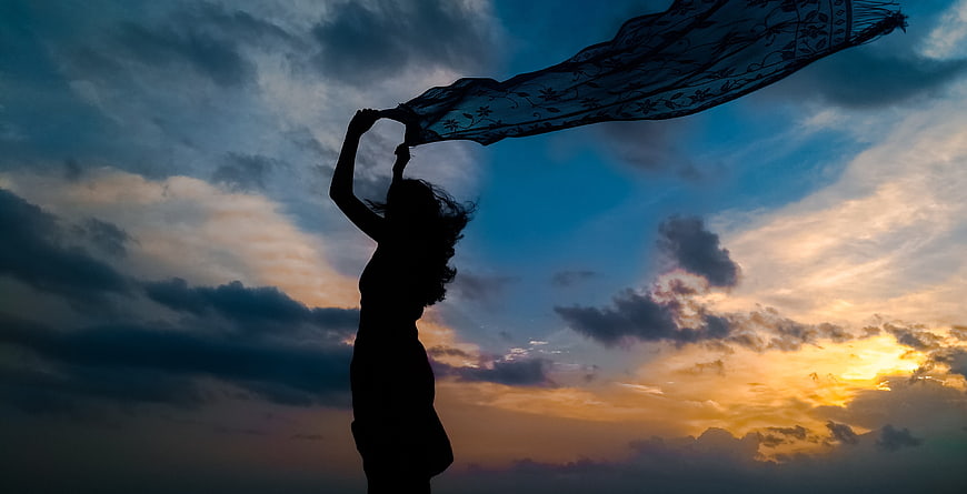 Silhouette of Woman Holding Scarf Against Dramatic Sunset Sky
