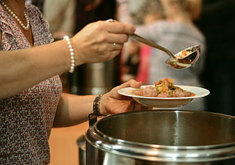 Woman serving vegetable soup from a large metal pot