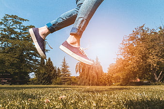 Woman Jumping In Park Wearing Sneakers And Jeans
