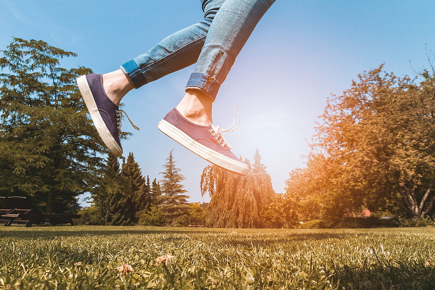 Woman Jumping In Park Wearing Sneakers And Jeans
