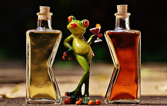 Funny frog figurine holding cocktail between two liquor bottles