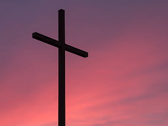 Silhouette of a cross against a pink and purple sunset sky