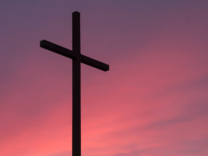 Silhouette of a cross against a pink and purple sunset sky