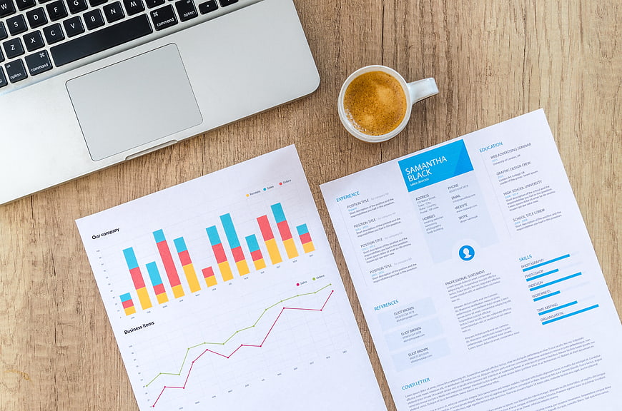 Flat lay of business resume, financial charts, laptop, and coffee on wooden desk