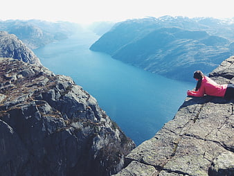 Woman in Pink Jacket Lying on Cliff Edge Overlooking Fjord