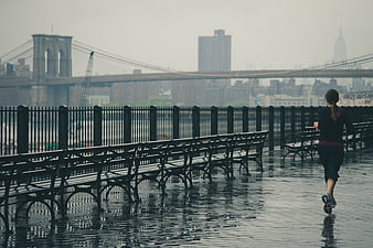 Woman jogging on wet promenade with Brooklyn Bridge background