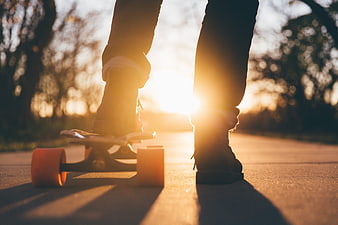 Skateboarder legs on asphalt path at golden hour sunset