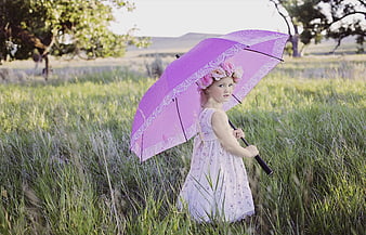 Young girl in white dress holding pink umbrella in grassy field