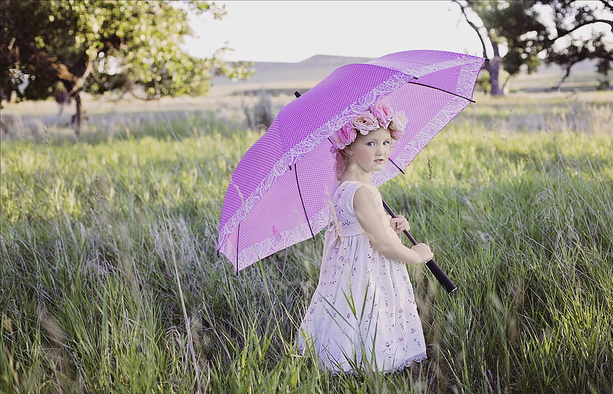 Young girl in white dress holding pink umbrella in grassy field