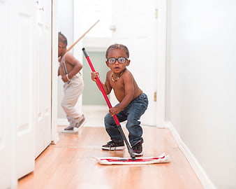 Toddler boy with glasses mopping wooden floor in hallway