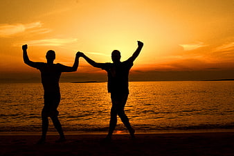 Silhouette of Two Men Celebrating on Beach at Sunset