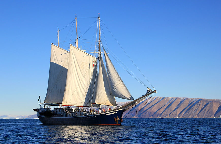 Historic sailing ship navigating icy waters near Greenland mountains