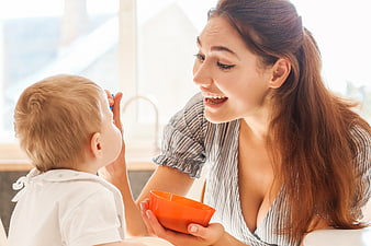 Happy mother feeding toddler baby with orange bowl