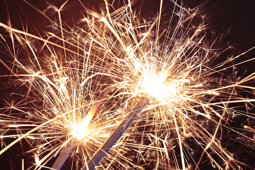 Close-up of burning sparklers with bright golden sparks on black background