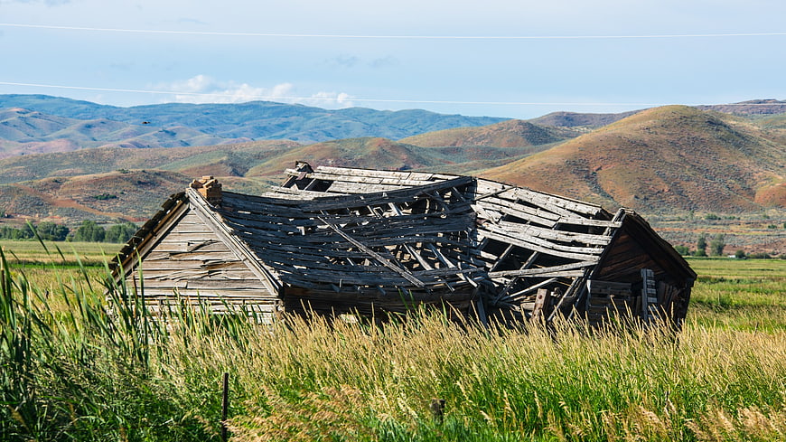 Dilapidated wooden barn in grassy field with mountains
