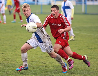 Two young soccer players competing for the ball on a muddy field